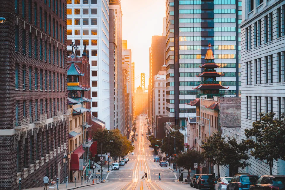 View down California Street in San Francisco, California with Chinatown pagoda buildings and golden hour sky in background.